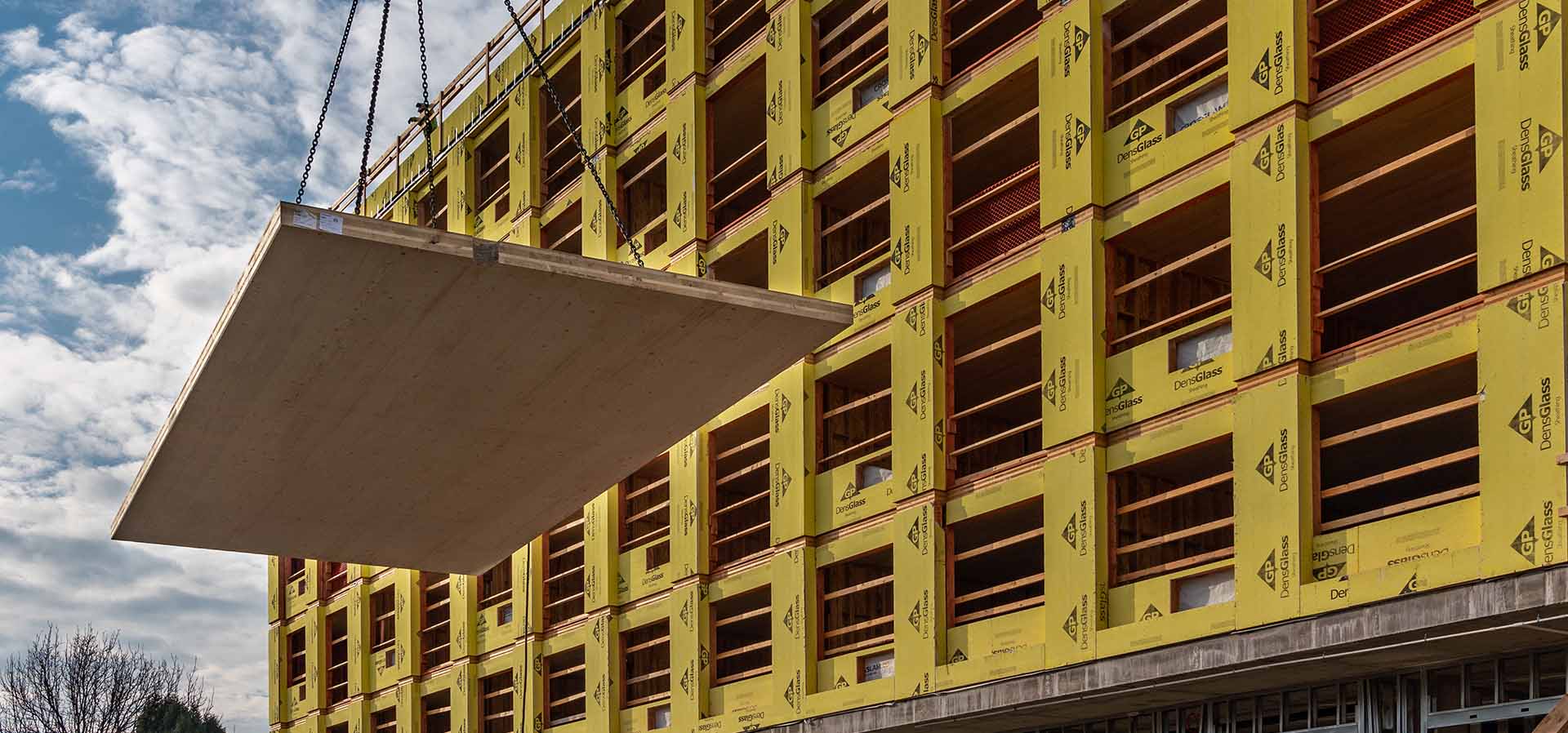 CLT panel being flown in on a crane in front of a mass timber building